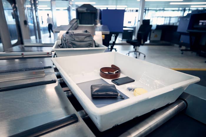 An airport security checkpoint tray holding a laptop, wallet, belt, phone, charger, and earphones on a conveyor belt