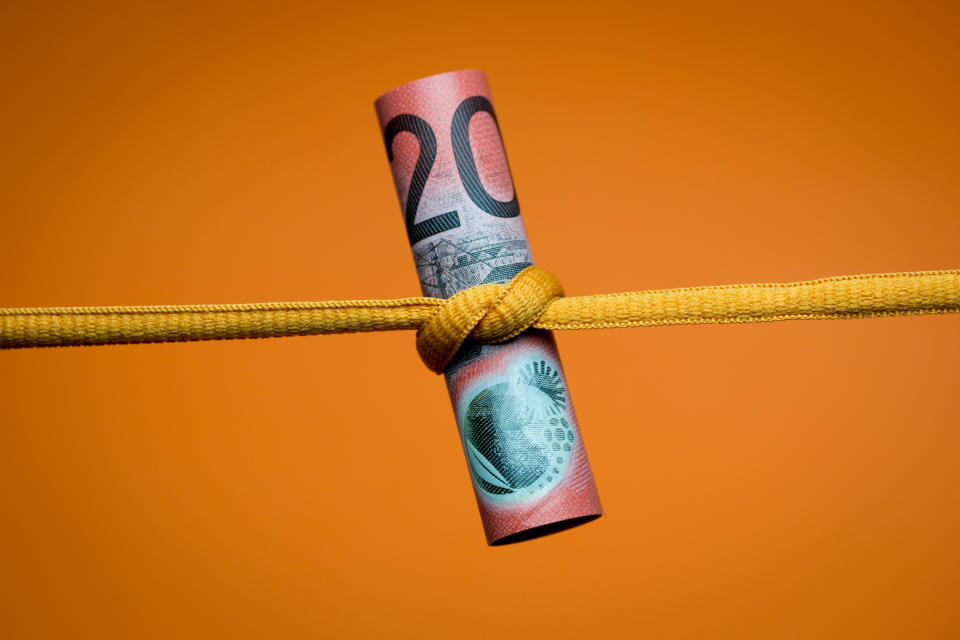 Close up of an Australian twenty dollar note tied in a knot. Studio shot on orange background.