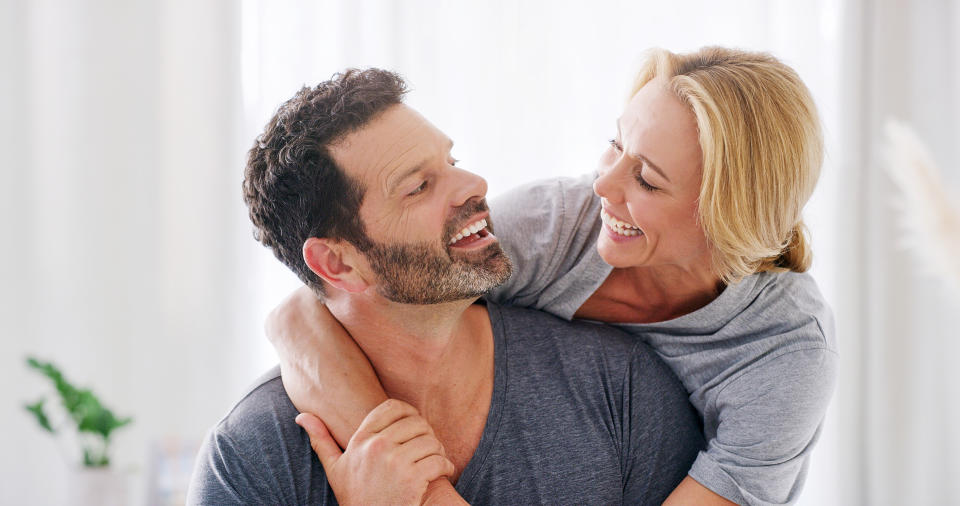 A man and a woman smiling at each other with the woman embracing the man from behind