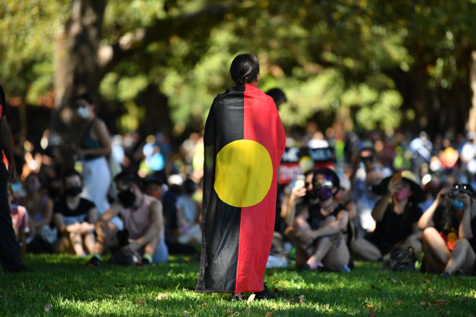 A woman stands draped in the Aboriginal flag in front of the crowd in Sydney. Source: AAP