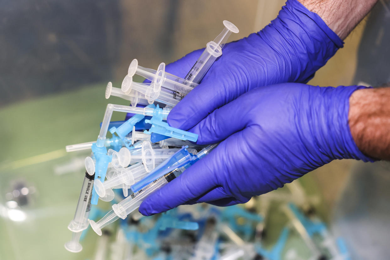 A member of the Thornton, Colo., Fire Department, wearing gloves, holds a handful of vials of Johnson & Johnson's COVID-19 vaccine.