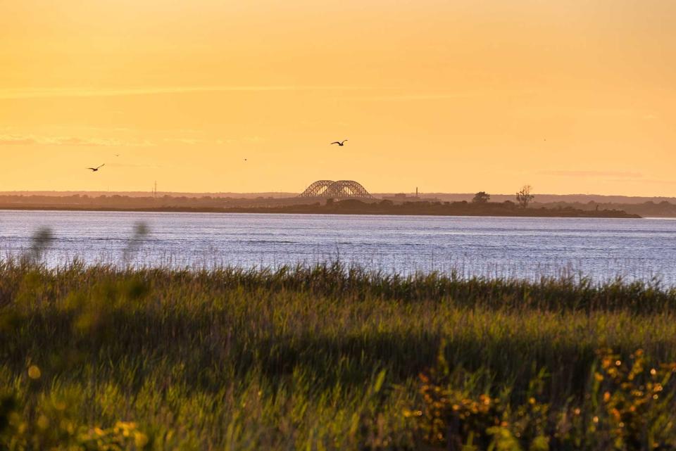 Golden sunset light above a long steel tied arch bridge - Robert Moses causeway