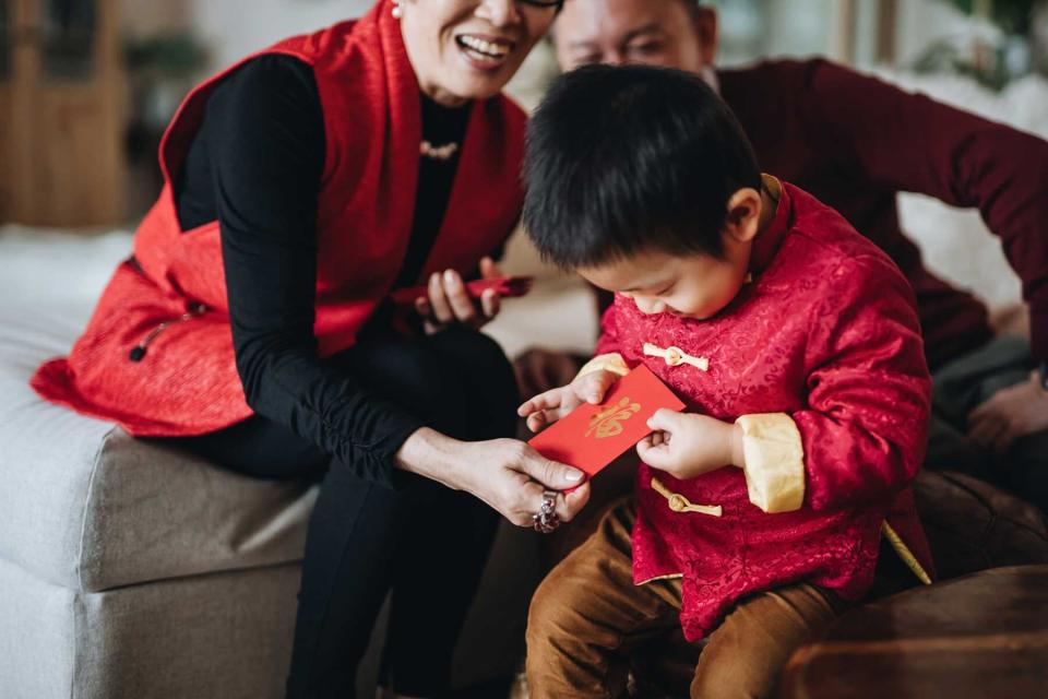 Grandson dressed in red traditional Chinese costume receives red envelops (lai see) with both hands from grandparents joyfully in Chinese New Year