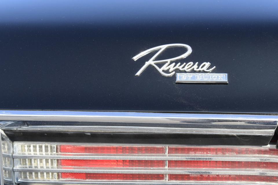 A chrome Riviera emblem above the taillights  on Carl Vandurmen's 1967 Buick. The sky reflecting on the shiny black paint makes it look blue.