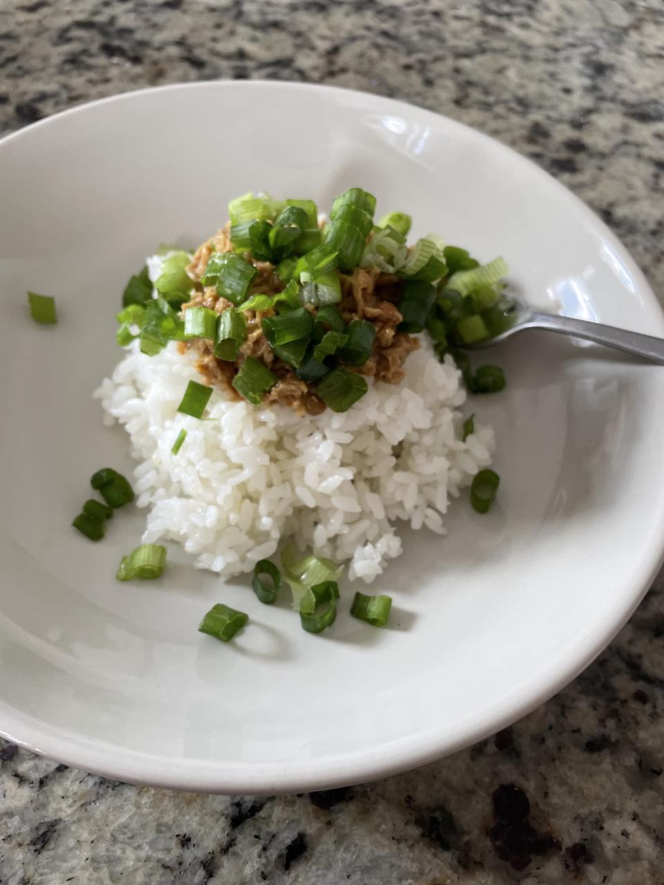 Bowl of white rice topped with natto and chopped green onions and a fork on the side on a granite countertop