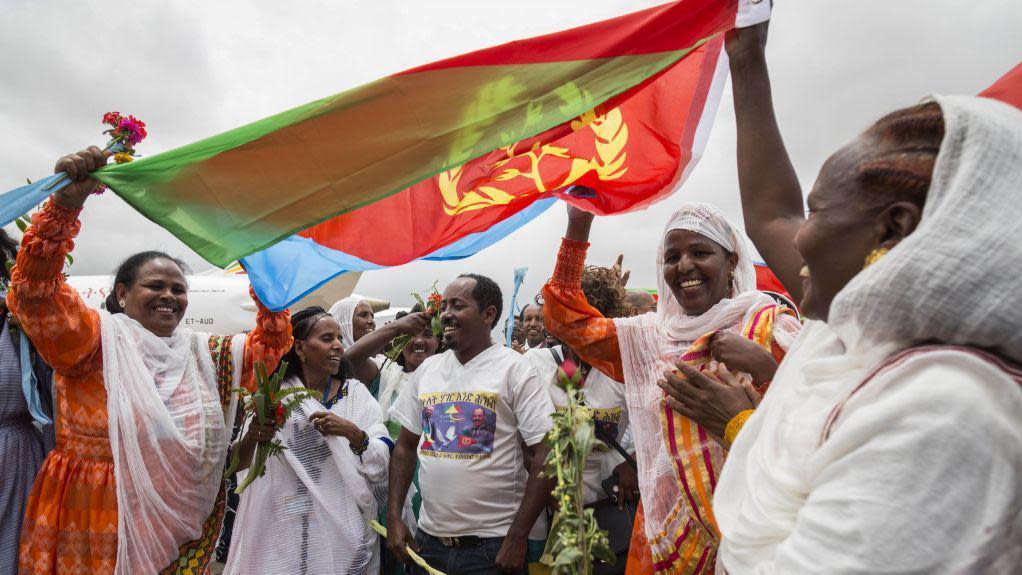 Eritrean women hold up the flag of Eritrea on July 18, 2018, to welcome passengers of the flight from Ethiopian capital Addis Ababa, upon their arrival at the Asmara International airport. - Ethiopia and Eritrea on July 18, 2018,