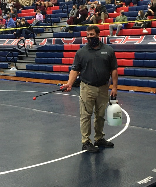 Effingham County wrestling coach Nico Guggino sprays sanitizer on mats before a match last season.