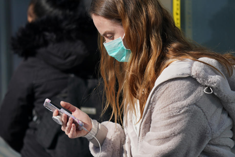 BERLIN, GERMANY - APRIL 27: A young woman wearing a face mask, who said she did not mind being photographed, looks at a smartphone as she waits at a tram at Alexanderplatz on the first day of a nationwide policy to wear protective face masks in stores and while riding public transportation during the novel coronavirus crisis on April 27, 2020 in Berlin, Germany. The German government is introducing steps to ease lockdown restrictions in order to help economic activity to resume while at the same time seeking to prevent a renewed surge in Covid-19 infections. (Photo by Sean Gallup/Getty Images,)