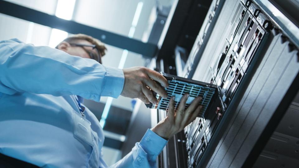 An engineer places a hard drive in a data center server tower.