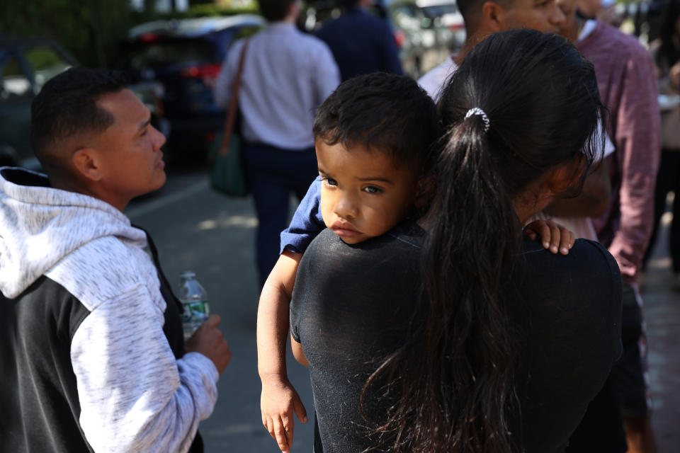 A toddler looks disconsolately over his mother's shoulder as a number of migrants wait to be fed.