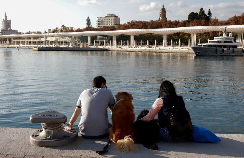 FILE PHOTO: People with their dogs enjoy the sun in front of the sea during unseasonably warm temperatures in Malaga