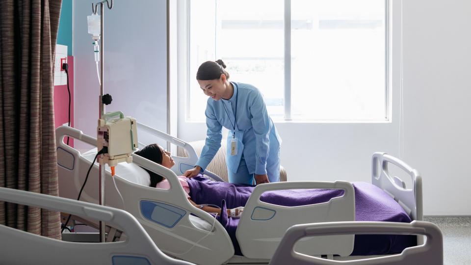 Mid adult pediatric professional checking young girl on ward, talking face to face.