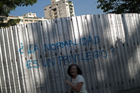 Belinda, a former teacher, laughs after taking a photograph of graffiti which reads 'Normality is a privilege?' in Caracas, Venezuela April 2, 2019. "We, the Venezuelan people, make a joke of everything," said Belinda. REUTERS/Ivan Alvarado