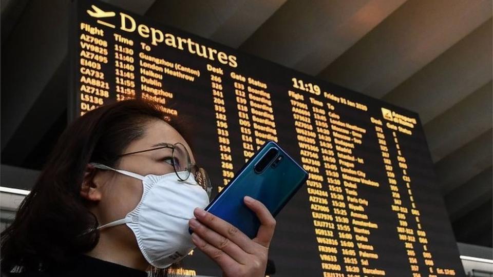 Una mujer con un teléfono frente a un tablero de aeropuerto