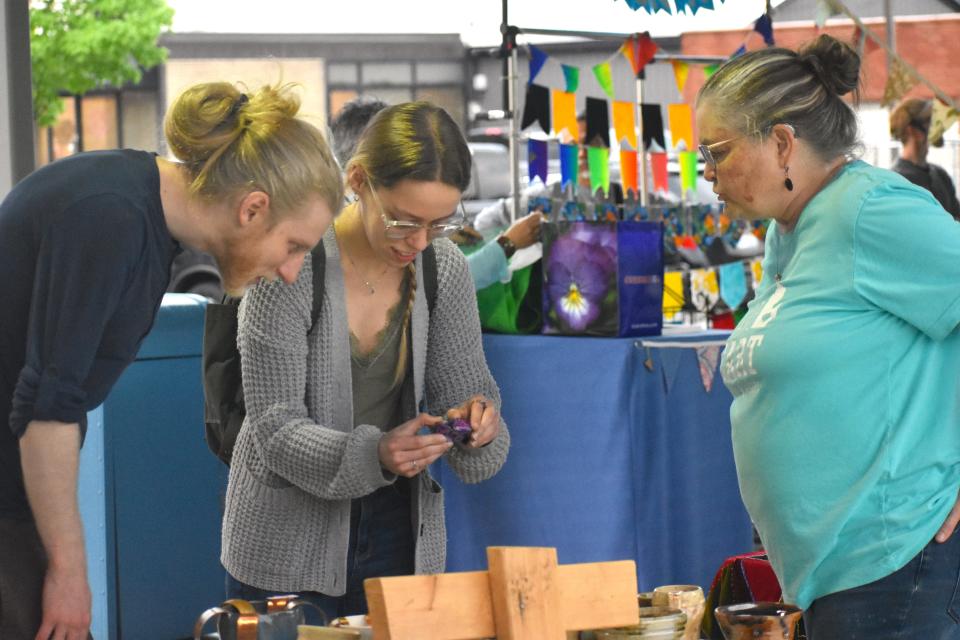 Blissfield residents Ryan Kremski and Carlee Wanless check out the jewelry and other crafts that were for sale by Annemarie Kallenbach, right, a local crafter specializing in pottery, jewelry, fiber and paper, during Saturday's grand opening of the Adrian City Market at the Pavilion in downtown Adrian. Kallenbach operates the small crafting business Come Home to Mamo.
