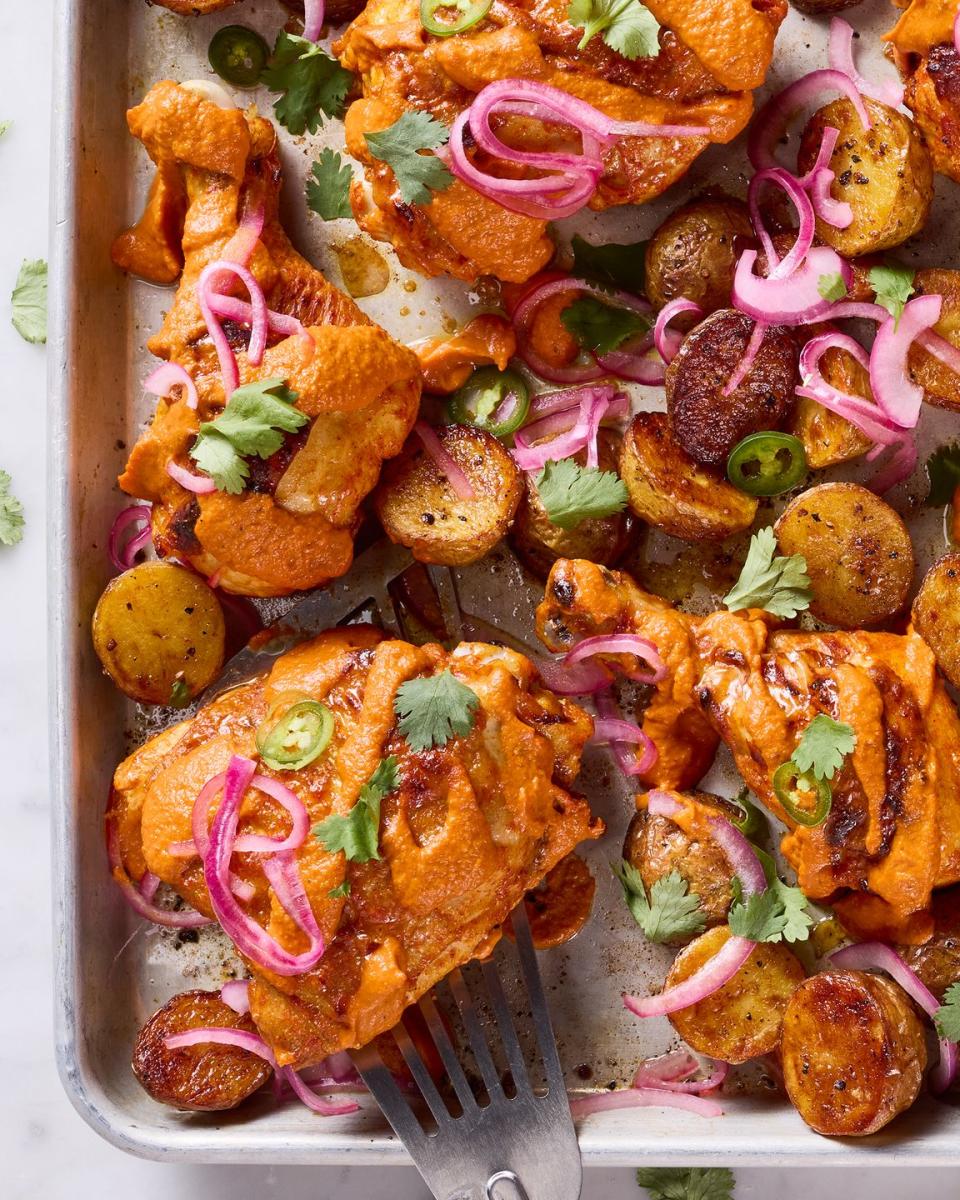 chicken thighs covered in a tikka masala sauce with pickled red onions and jalapenos on a sheet pan