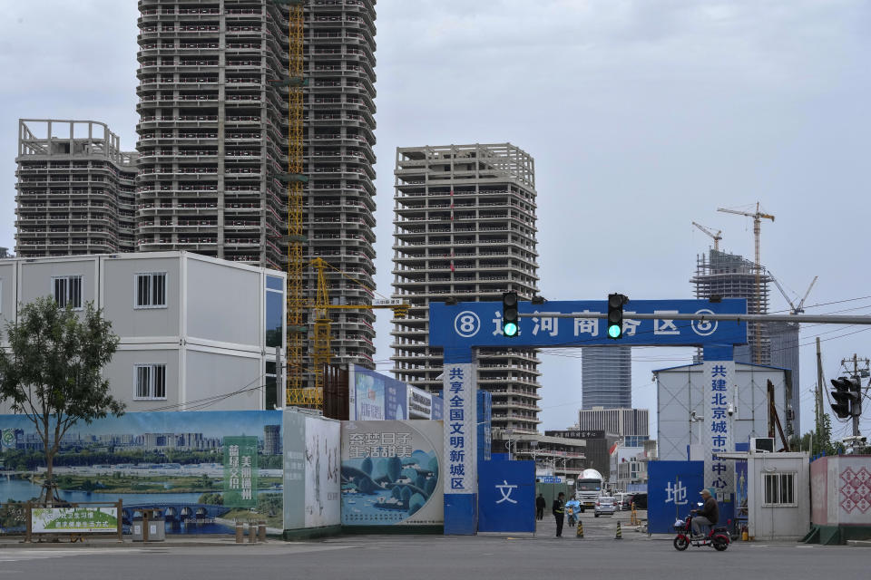 A man rides a scooter past by a security guard on duty at an entrance gate of a commercial office buildings under construction in Tongzhou, outskirts of Beijing, Monday, Oct. 4, 2021. China’s economy is losing steam as President Xi Jinping's government cracks down on corporate debt and energy use in pursuit of more stable, sustainable growth. (AP Photo/Andy Wong)