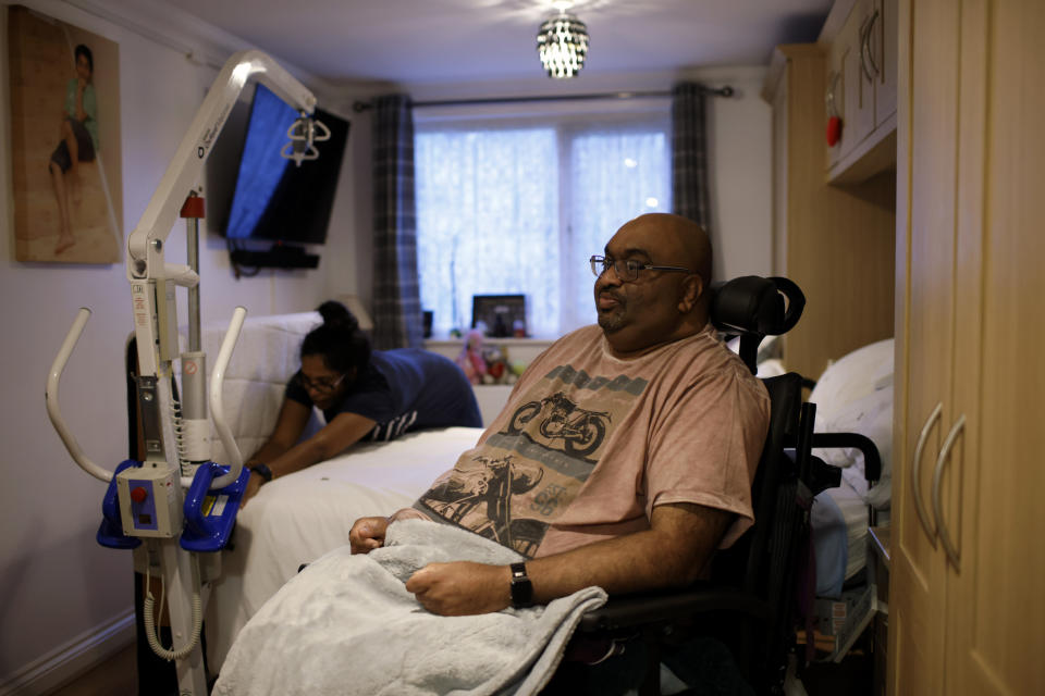 Thirugnanam Sureshan, 50, whose disabilities require round-the-clock care and present difficulties coping with cost of living increases, sits in his bedroom as his wife Sridevi, 46, makes the bed at their home in Bexhill, East Sussex, England, Wednesday, Nov. 9, 2022. Sureshan has a rare condition called Charcot foot which affects the bones, joints and tissues in his foot. He also has thyroid problems and an eye condition. Because of his condition, he doesn't cope well with the cold. (AP Photo/David Cliff)