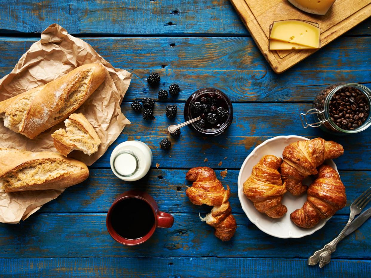 Fresh baked croissants and baguette, blackberry jam, coffee and cheese on old wooden table