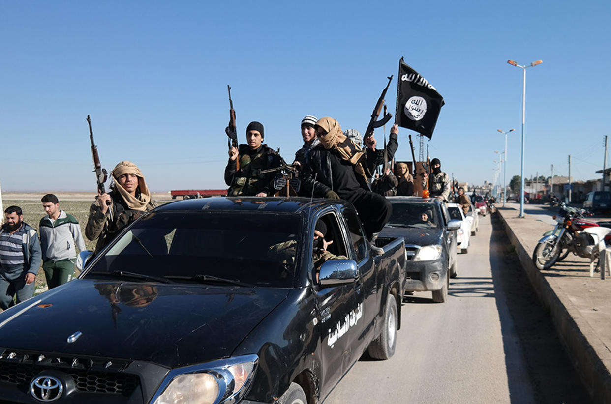 In this photo released on May 4, 2015, by a militant website, which has been verified and is consistent with other AP reporting, Islamic State militants pass by a convoy in Tel Abyad town, northeast Syria. (Militant website via AP)