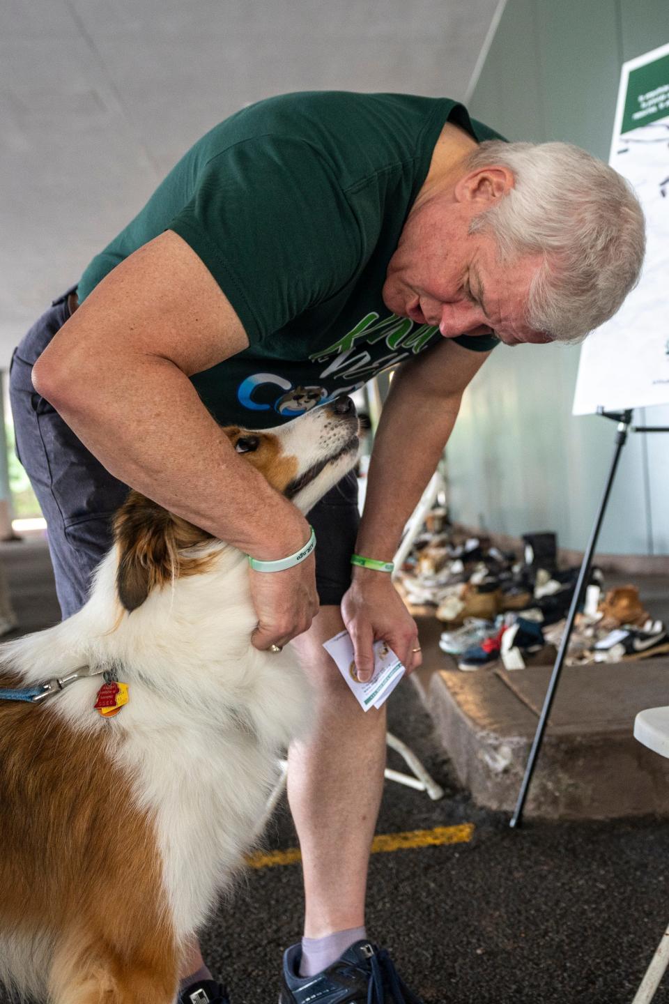Kurt Baker, one of the founders of the "In Their Shoes" exhibit, pets Murphy, a therapy dog in training, in Woodland Park on Saturday, September 9, 2023. Each pair of shoes represents a young New Jersey resident who died by suicide. Baker and his wife, Tricia Baker (not shown) started the exhibit after their son Kenny died by suicide.