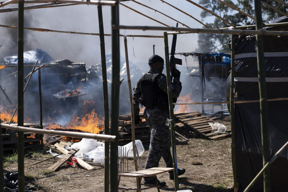 A police officer walks past tents and shacks consumed by fires caused by stoves that were left unattended during an eviction at a settlement coined the "First of May Refugee Camp," named for the date people moved on the land designated for a Petrobras refinery, in Itaguai, Rio de Janeiro state, Brazil, Thursday, July 1, 2021, amid the new coronavirus pandemic. (AP Photo/Silvia Izquierdo)