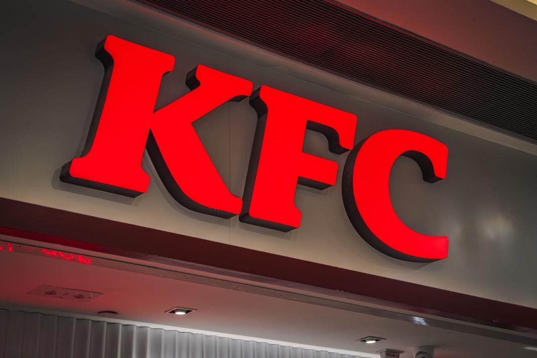 A brightly illuminated red KFC logo on a store facade, highlighting the iconic brand during the evening. The image focuses on visual branding and corp