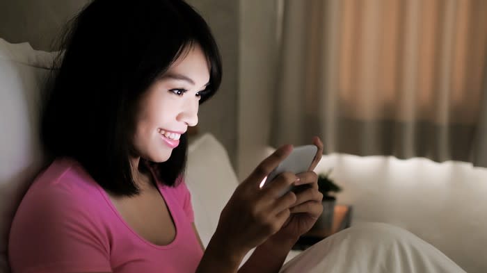 A young woman sitting up in bed and using her smartphone.