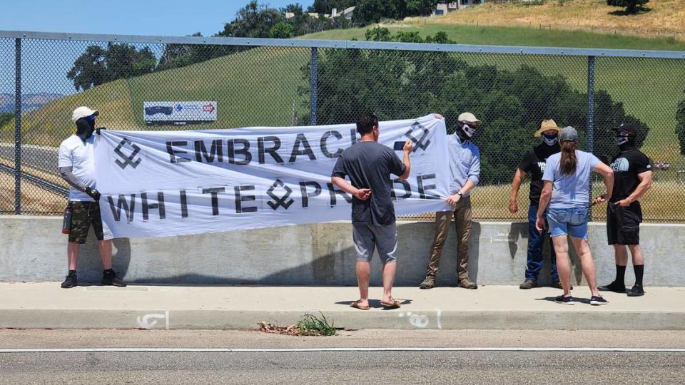 Several men with masks hold up an “Embrace white pride” flag on the Vineyard Drive Highway 101 overpass on Saturday, May 13, 2023.