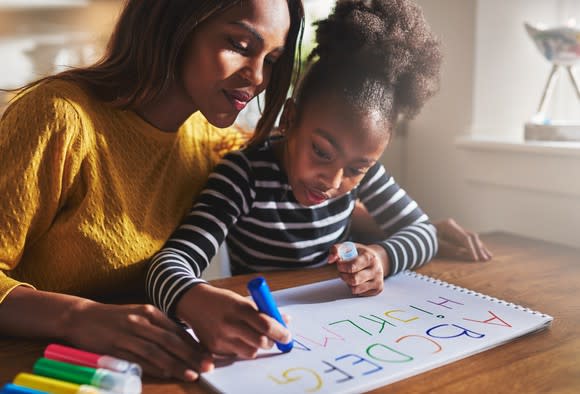 Young girl writing the alphabet while mother watches