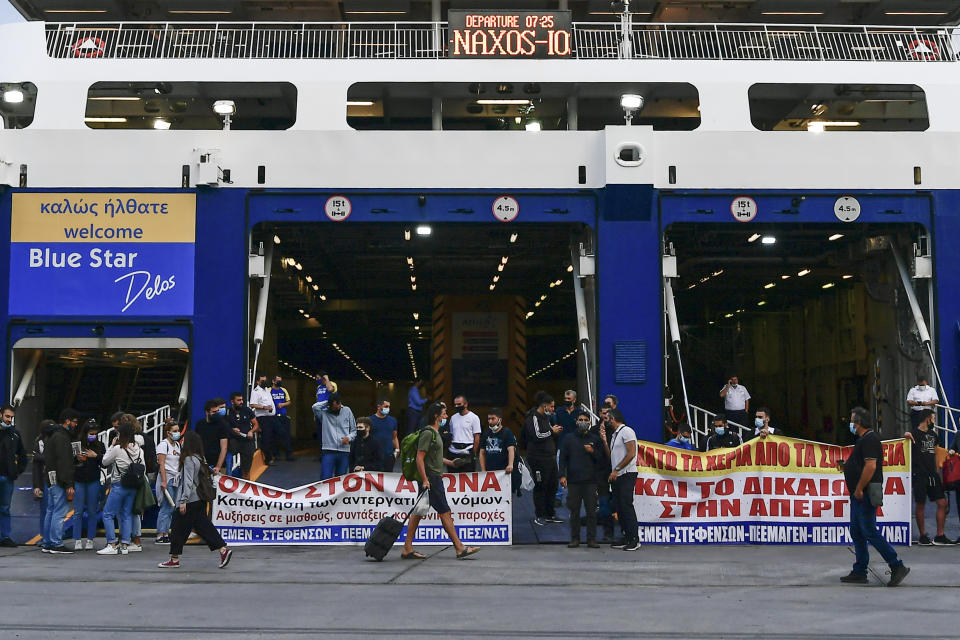 A passenger walks past protesters blocking the entrance of a passenger ferry during a 24-hour labour strike at the port of Piraeus, near Athens, Thursday, June 10, 2021. Greece's biggest labor unions stage a 24-hour strike to protest a draft labor bill being debated in parliament, which workers say will erode their rights. (AP Photo/Michael Varaklas)