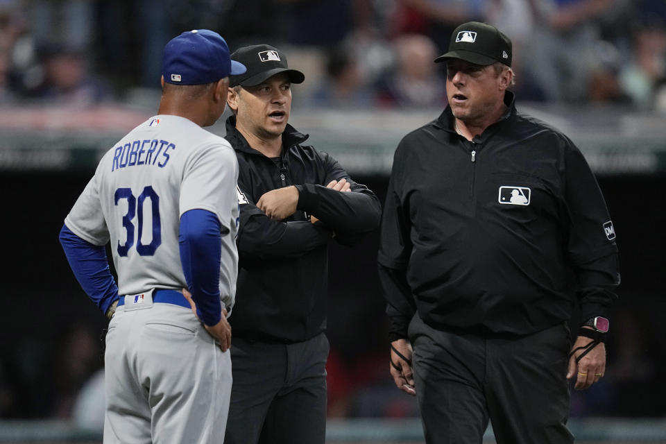 Los Angeles Dodgers manager Dave Roberts (30) talks with umpires Mark Wegner, center, and Bruce Dreckman as the game between the Dodgers and the Cleveland Guardians is delayed in anticipation of rain, in the third inning Wednesday, Aug. 23, 2023, in Cleveland. (AP Photo/Sue Ogrocki)