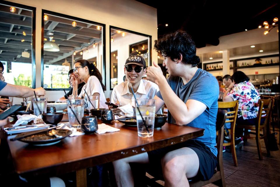 A group of young people smiling and laughing around a table at a restaurant.