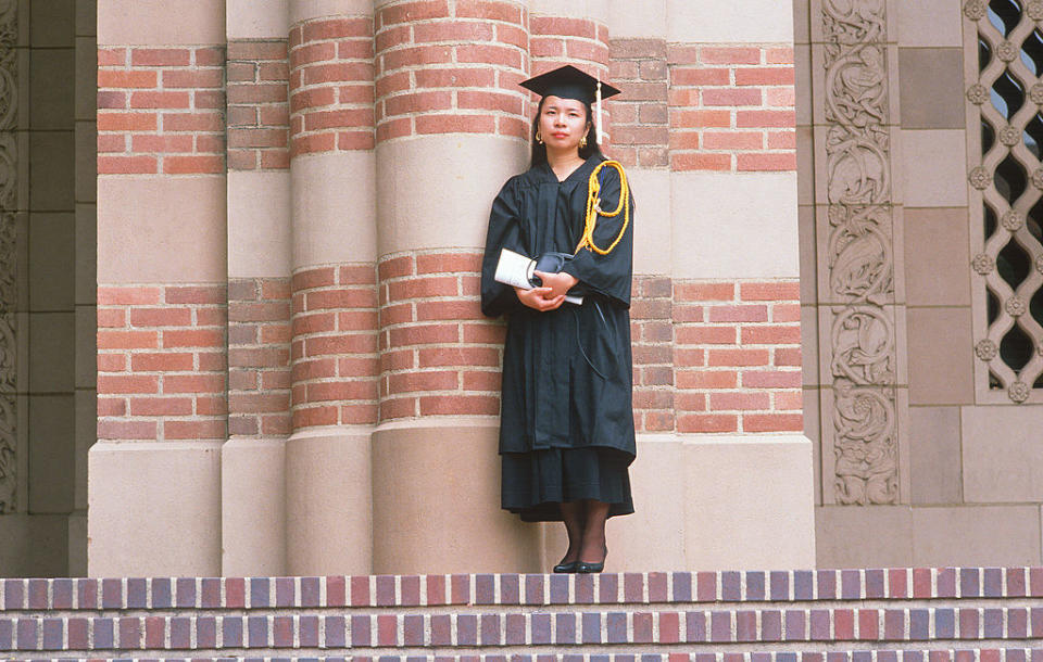 A college graduate stands alone against the exterior of a university building