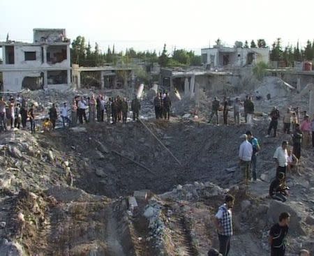 People gather around a crater in Homs city June 20, 2014, in this picture released by Syria's national news agency SANA. REUTERS/SANA/Handout via Reuters