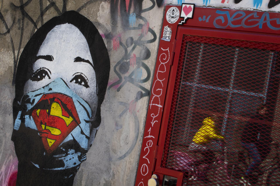 A mother and her child are reflected as they pass a mural by artist FAKE, titled "Super Nurse", paying tribute to all healthcare and medical professionals in times of the coronavirus, in Amsterdam, Netherlands, Sunday, April 19, 2020. (AP Photo/Peter Dejong)