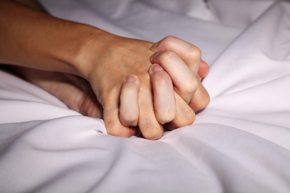 Two hands entwined in bed (Getty Images)