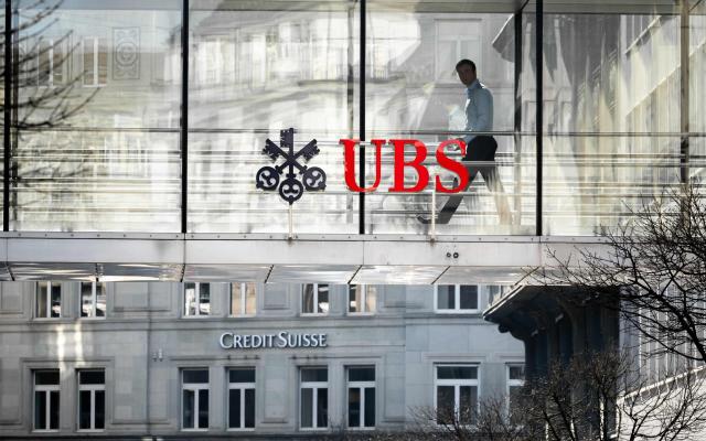 A employee is seen in silhouette next to a sign of Swiss giant banking UBS and a sign of Credit Suisse bank in Zurich - FABRICE COFFRINI/AFP via Getty Images