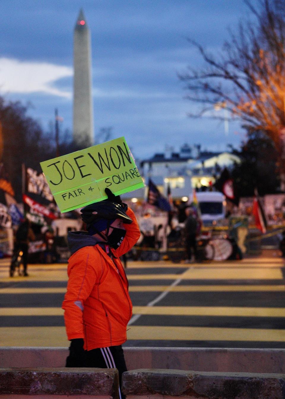 A silent protester holds a sign in support of President-elect Joe Biden‘s victory as he marches Monday night in Black Lives Matter Plaza in Washington, D.C.