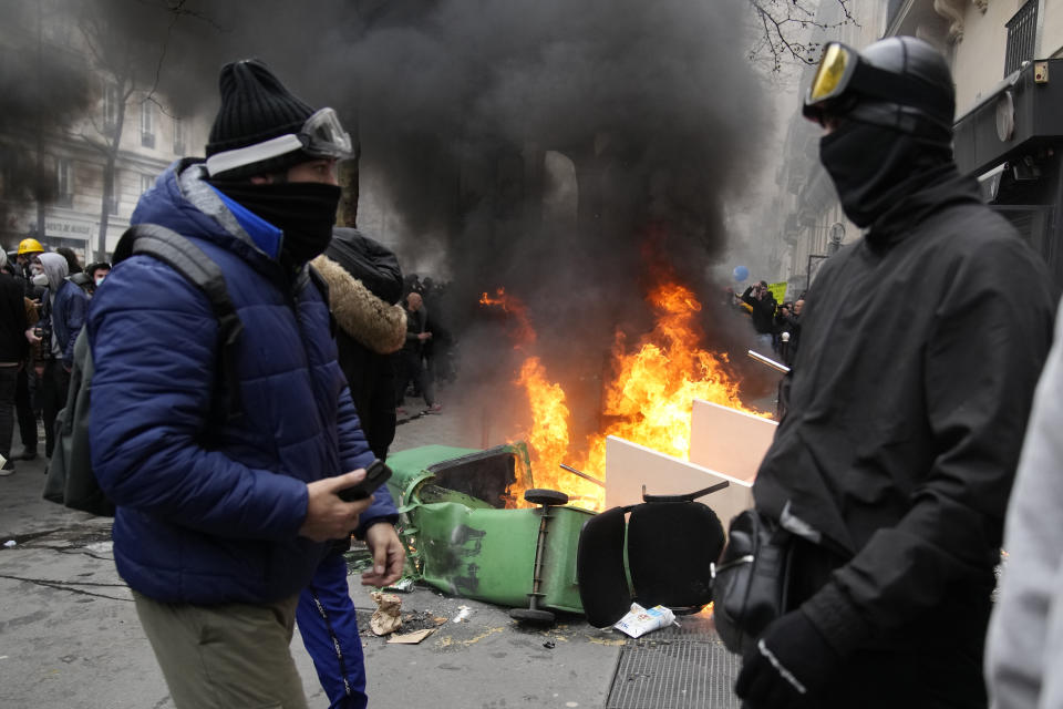 Youths stand by burning garbage cans during a demonstration Tuesday, March 28, 2023 in Paris. It's the latest round of nationwide demonstrations and strikes against unpopular pension reforms and President Emmanuel Macron's push to raise France's legal retirement age from 62 to 64. (AP Photo/Christophe Ena)