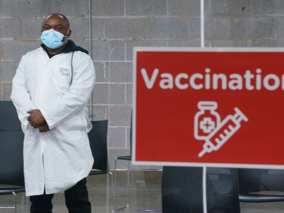 A health-care worker waits for patients at a COVID-19 vaccination clinic in Montreal's Olympic Stadium in February of 2021. As of October Quebecers will be able to get both the flu and the COVID-19 vaccine in one stop at a vaccination clinic.  (Paul Chiasson/The Canadian Press - image credit)