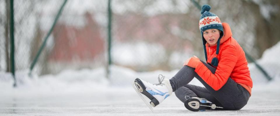 Ice skating concept - young woman sitting on the ice rink after falling down and hurting her knee