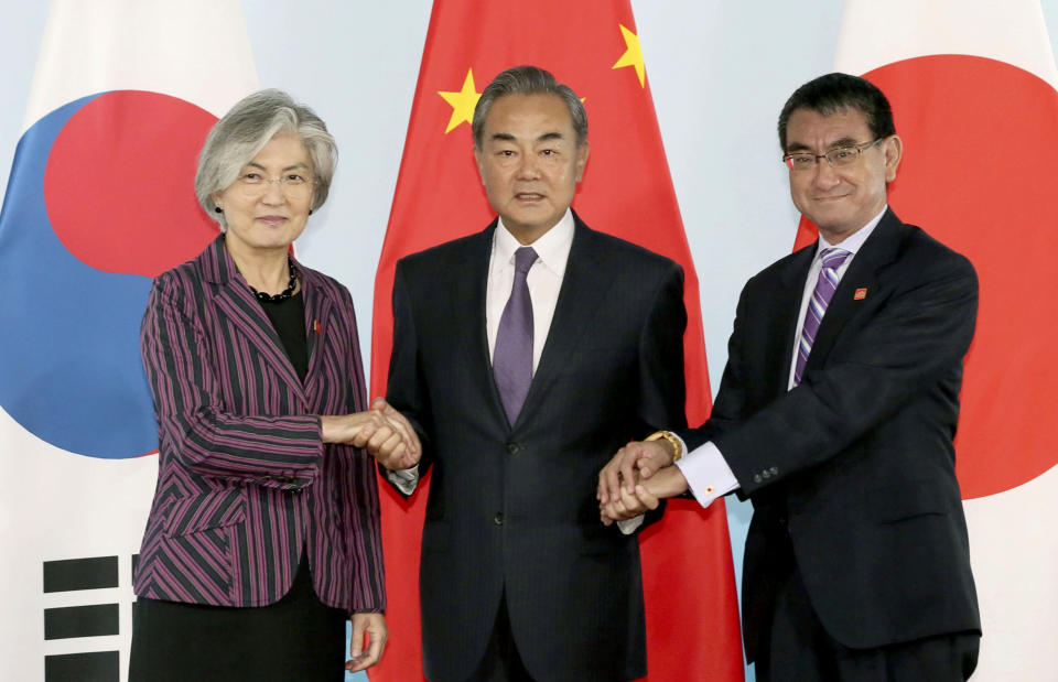Chinese Foreign Minister Wang Yi, center, holds hands of his South Korean counterpart Kang Kyung-wha, left, and Japanese counterpart Taro Kono for photos ahead of their meeting in Beijing Wednesday, Aug. 21, 2019. (Kyodo News via AP)