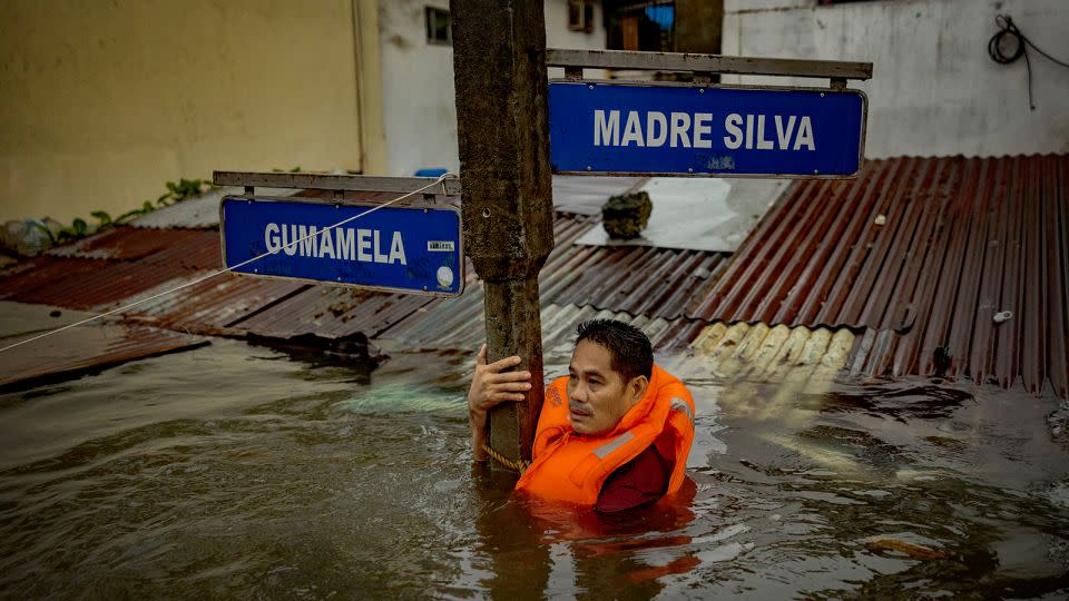 A resident holds on to a street sign in a road flooded by Typhoon Gaemi and monsoon rains on July 24, 2024 in Quezon City. - Ezra Acayan/Getty Images