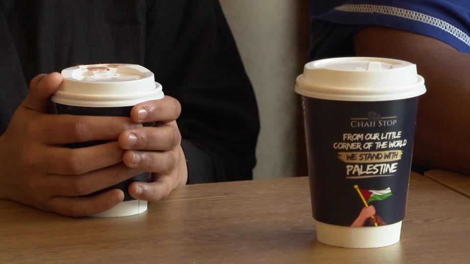 Woman holds cup on table with message supporting Palestine written on the packaging. 