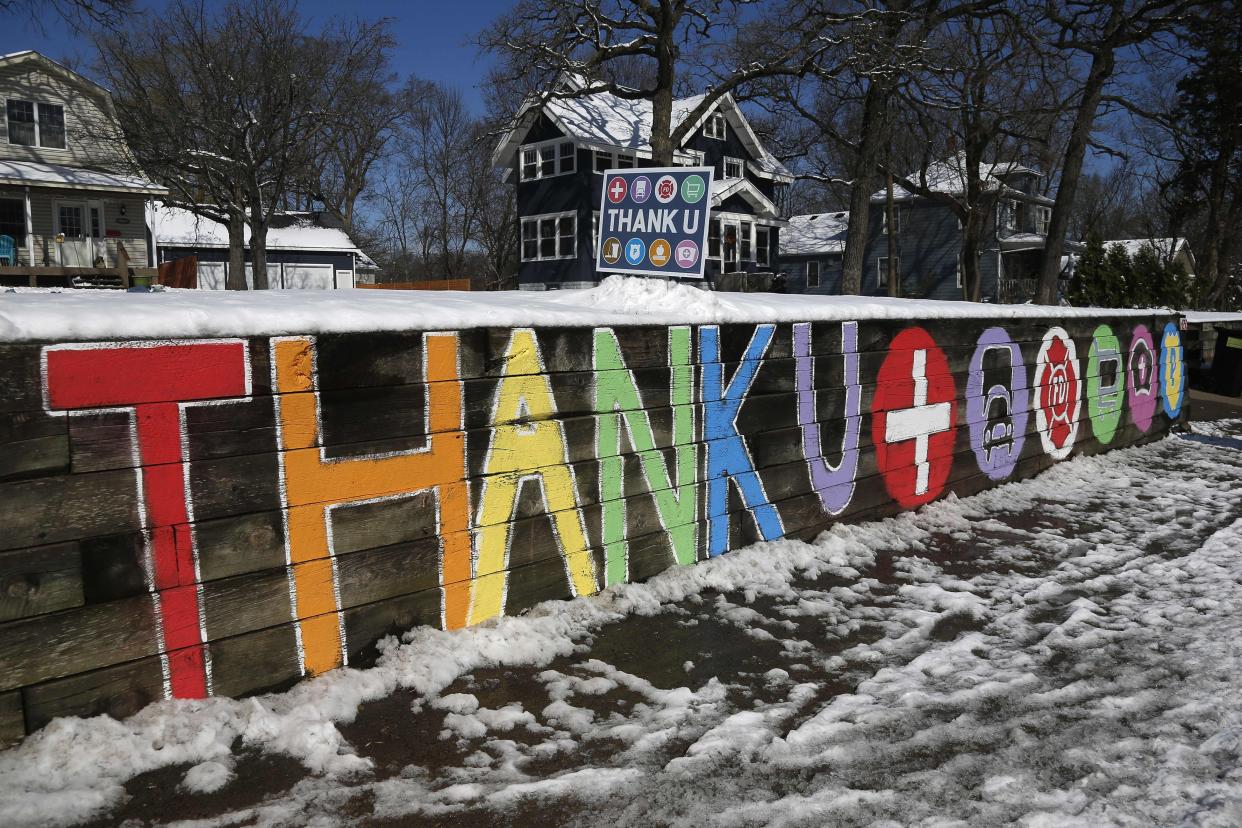 A wooden retaining wall message in front of a home, left, offers thanks to health professionals and first responders for their responses in the fight against the coronavirus on Monday, April 13, 2020, in Edina, Minn.