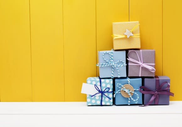 Six wrapped presents stacked in a pyramid shape against a yellow wall.