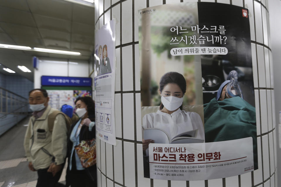 People wearing face masks to help protect against the spread of the coronavirus walk by a poster informing mandatory mask wearing at a subway station in Seoul, South Korea, Sunday, Sept. 20, 2020. South Korea's new coronavirus tally has fallen below 100 for the first time in more than a month. The banner reads: " Which mask would you wear?" (AP Photo/Ahn Young-joon)