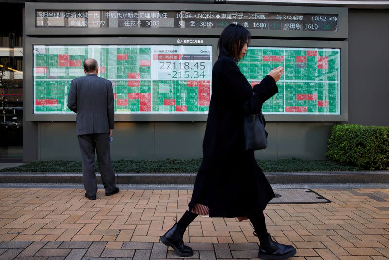 FILE PHOTO: A woman walks past a man examining an electronic board showing Japan's Nikkei average and stock quotations in Tokyo