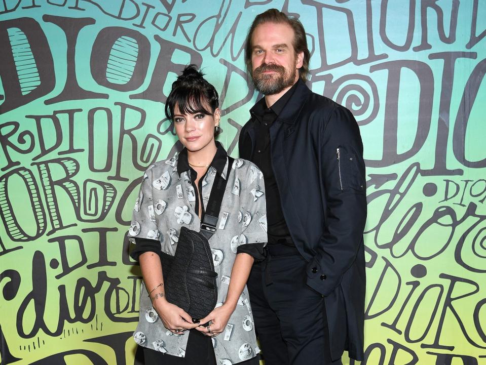 Lily Allen, in a black printed blouse and black dress, poses on the red carpet with David Harbour, in a black suit, in 2019.